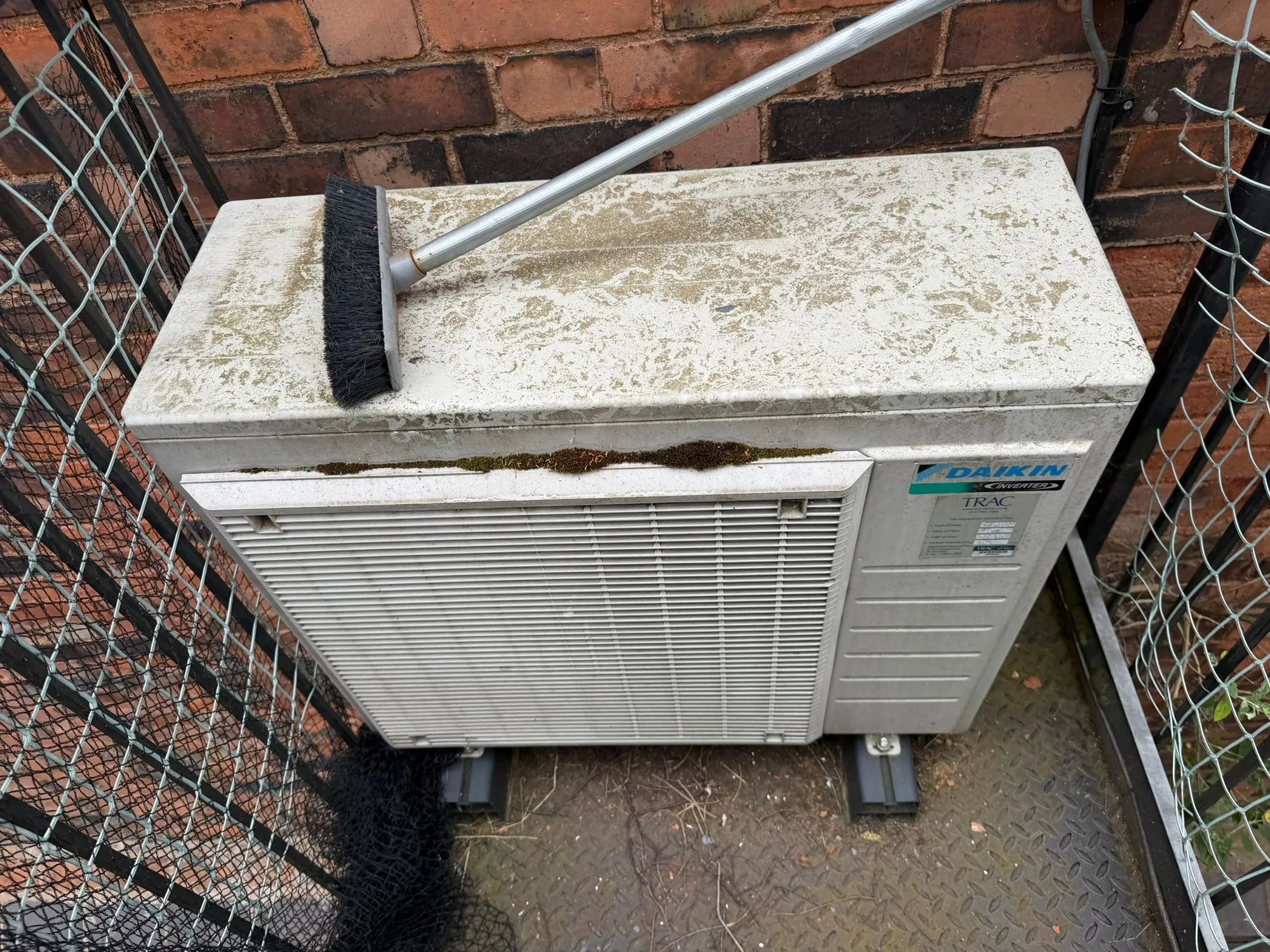 Outdoor air conditioning condenser covered in moss and dirt being cleaned during a maintenance visit by Aervue